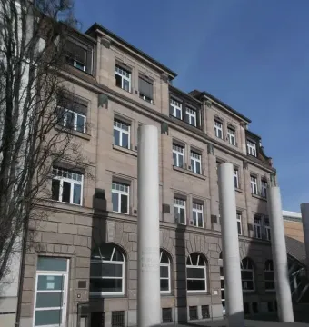 Tall white pillars of the Way of Human Rights stand in front of a stone building with many windows.