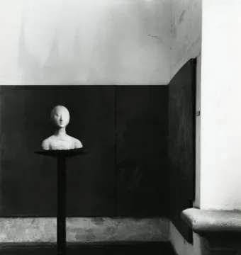 Portrait of Eleanor of Aragon, a pale bust on a slender dark stand against a dark wall.