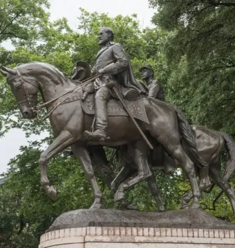 Bronze equestrian sculpture of Robert E. Lee with a second figure behind him, set against trees and an overcast sky.