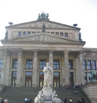 Schiller Monument with seated allegorical figures at its base in front of a classical building.