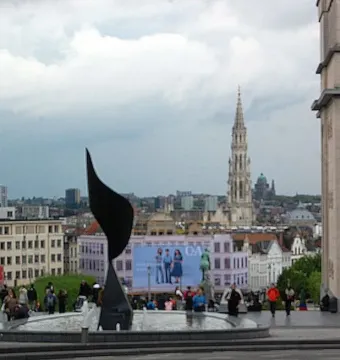 The Whirling Ear sculpture in a circular fountain in a public plaza, with a city spire in the background.