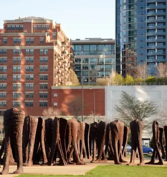 Agora sculpture in Grant Park, with tall dark headless figures standing on a paved and grassy area against Chicago buildings.