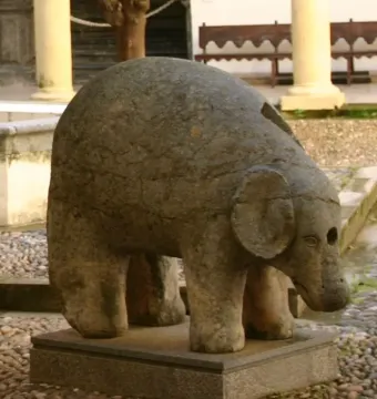Weathered stone Elephant Fountain sculpture with rounded ears on a rectangular base in a courtyard.