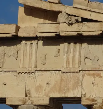 Fragmentary Parthenon pediment stonework with carved horse figures against a blue sky.