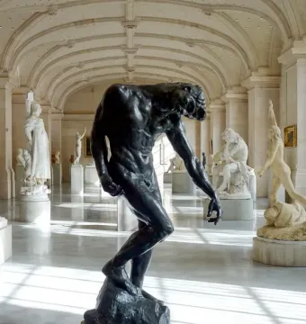 The Shade, a dark muscular nude male sculpture with a hunched posture and bowed head in a museum hall.