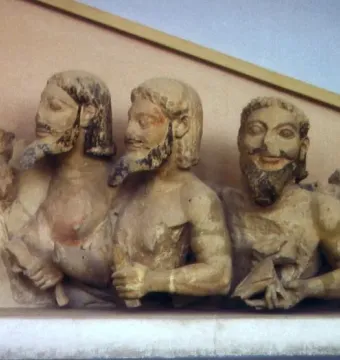 Trisomatos Typhon carved in light-colored stone with three bearded heads and traces of original pigment.