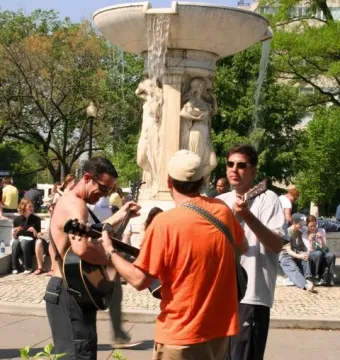 Dupont Circle Fountain with water flowing from the upper bowl and people gathered around it, including musicians in the foreground.
