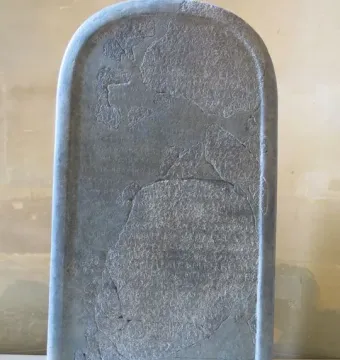 Mesha Stele, a tall dark stone slab covered in ancient carved script with missing fragments and visible cracks.