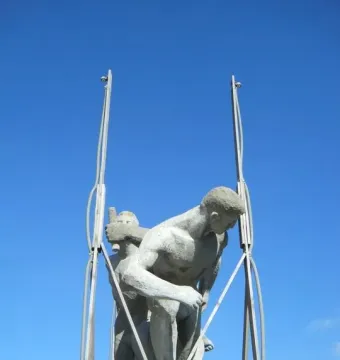 Sztafeta sculpture showing two nude male figures against a blue sky, with metal supports around the figures.