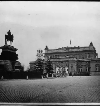 The Tsar Liberator Monument stands on an ornate pedestal in a wide square, with a classical building and domed structure behind it.