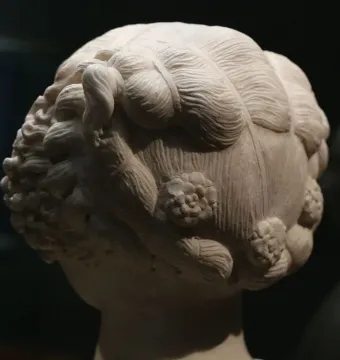 Bust of a Young Woman showing the back and side of the sculpted head with an elaborate wavy hairstyle and carved rosette motifs.
