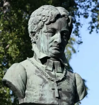 Weathered green statue of Frans Michael Franzén in clerical vestments with a crucifix necklace.
