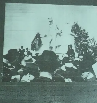 Crowd gathered around the Monument to Giuseppe Gioachino Belli, with a tall statue of a man in a top hat at the center.