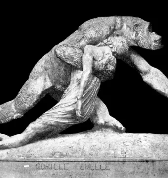 Black-and-white photograph of the sculpture Gorilla Carries a Woman, showing a gorilla striding forward with an unconscious woman draped over its back.