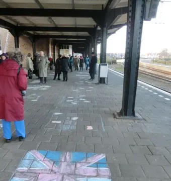 People gathered on a train station platform near the Kindertransport monument, with a large pink and blue chalk Union Jack drawn on the ground.