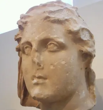 Lycosoura Demeter stone head with weathered features on a gray pedestal.