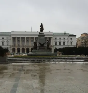Tadeusz Kościuszko Monument on a stone pedestal in front of a white columned building in Warsaw.