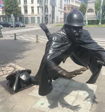 Vaartkapoen bronze sculpture showing a uniformed policeman falling as a figure emerges from an open manhole and grabs the cover.