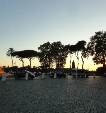 Monument to Giuseppe Garibaldi lit by warm light above a cobbled plaza, with parked cars and silhouetted trees at sunset.