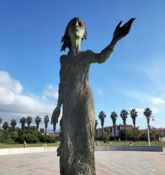 La madre del emigrante bronze statue of a woman standing barefoot with one arm outstretched in a plaza