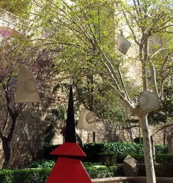 Alexander Calder’s Nancy sculpture with a dark red and black geometric base and weathered metal arms in a park setting.