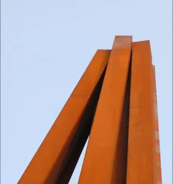 Neuf Lignes Obliques sculpture with tall rusty orange metal beams rising at sharp angles against a pale sky.
