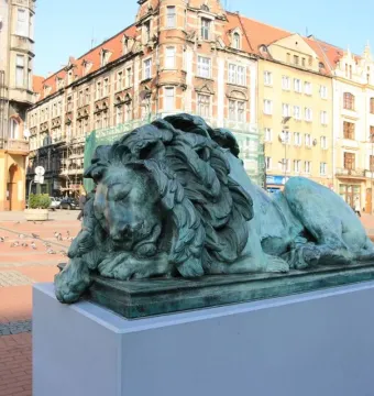 Sleeping Lion bronze statue with a green patina on a gray pedestal in a town square.