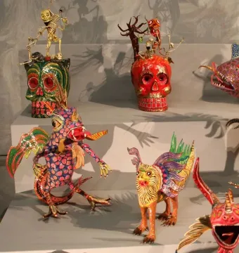 Colorful alebrije sculptures with hybrid creature features and decorated skulls on tiered platforms.
