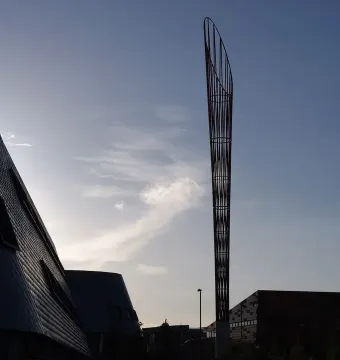 Aspire sculpture silhouetted against a bright, partly cloudy sky near modern campus buildings.