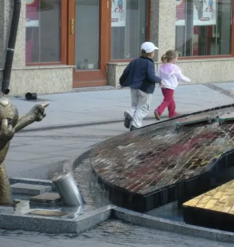 Reksio Monument beside a modern fountain, with a bronze dog figure standing in a shallow pool.
