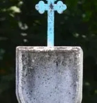 Weathered stone Padrão monument with a shield carving and blue cross, standing in grass and foliage.