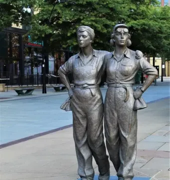 Women of Steel sculpture showing two female figures standing arm in arm on a paved walkway.