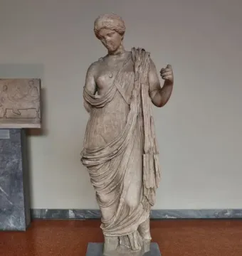 Armed Aphrodite marble statue on a pedestal in a museum gallery.