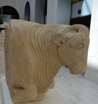 Bull of Osuna stone sculpture with carved bull head and forequarters displayed in a museum gallery.