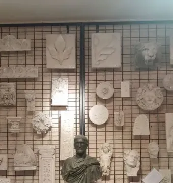 Capitoline Brutus bronze bust on a black pedestal, shown in front of a wall of plaster casts.