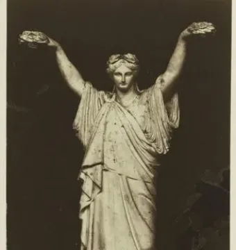 Sepia studio photograph of France crowning Art and Industry, showing a draped female figure with both arms raised on a stepped pedestal.