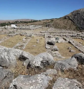 A greenish stone block stands among the ruins at Hattusa, surrounded by scattered ancient foundations and grey masonry.