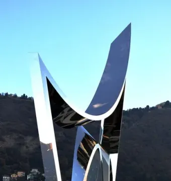 Life Electric sculpture with reflective silver panels against blue sky and distant hills.