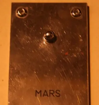 Brushed metal Mars plaque with engraved lettering, numeric data, and a small spherical detail.