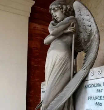 Monteverde Angel, a winged stone angel with bowed head and crossed arms holding a long staff, standing on a tiered base.