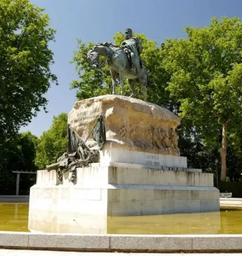 Monument to General Martínez-Campos with an equestrian bronze statue on a tiered stone pedestal in a pool surrounded by trees.