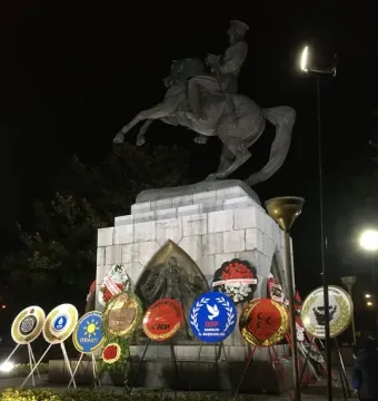 The Statue of Honor illuminated at night, with wreaths and placards arranged around its pedestal.