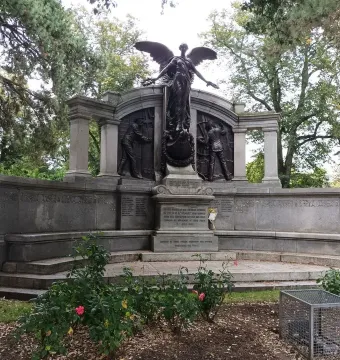 Titanic Engineers\' Memorial with a winged female figure above bronze relief panels in a park setting.