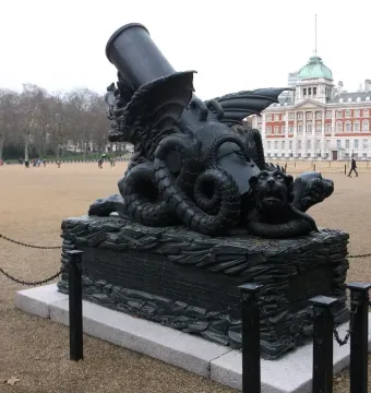The Cádiz Memorial stands on Horseguards Parade, with an ornate dark sculptural base and a cannon-like barrel rising upward in front of a large classical building.
