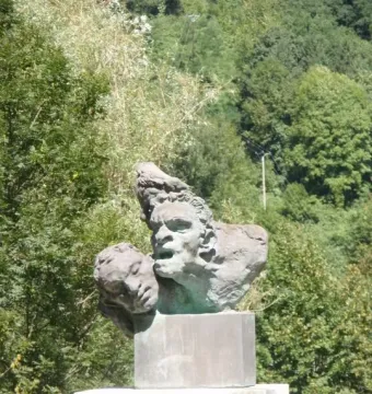 Capoulet-et-Junac war memorial with a bronze sculpture on a tall stone pedestal against a wooded hillside.