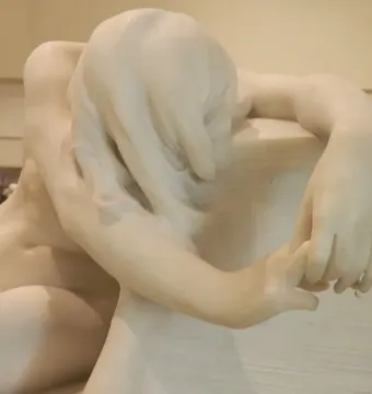 Desolation, a white marble sculpture of a bowed figure with an outstretched hand resting on a textured block.
