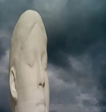 The Dream sculpture, a pale segmented head and neck with closed eyes, stands against dark cloudy skies.