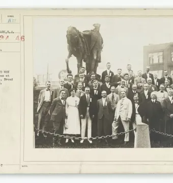 A large group of men and one woman pose in tiers in front of the George Washington monument.
