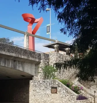 La Antorcha de la Amistad rising above a stone wall beside the riverwalk under a blue sky.