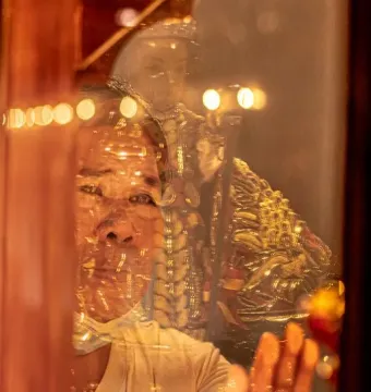 Santo Niño de Cebú in gold-toned robes with a person’s face and outstretched hand reflected over the image.